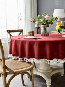 Close-up of deep red linen-textured round tablecloth with white cotton tassel fringe