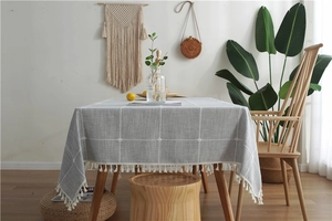 Detailed close-up of grey plaid tablecloth with elegant white cotton tassel fringe