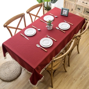 Detail of burgundy linen-textured tablecloth featuring ivory tassel edges on wooden table