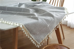 Close-up of light grey and white plaid tablecloth texture with delicate cotton fringe trim
