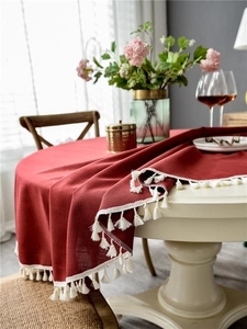 Close-up of deep red linen-style tablecloth with cream fringe edge on a round table