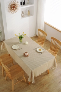 Close-up of beige striped rectangular tablecloth with elegant fringe tassels and linen texture