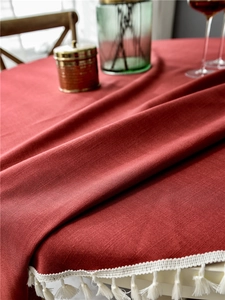 Close-up of deep red tablecloth featuring woven fabric texture and white tassel fringes