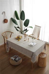 Detail of grid embroidered tablecloth with white tassel edges on wooden table