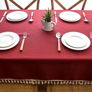 Detail of red faux linen tablecloth with creamy white tassel trim on a dining table