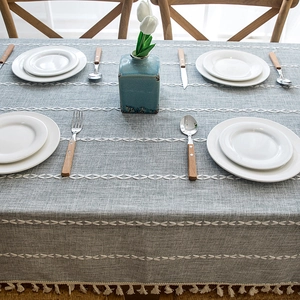 Close-up of gray faux linen tablecloth with white geometric embroidery and fine tassels