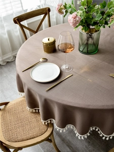 Detail view of brown linen round tablecloth with white tassel edge on wooden table