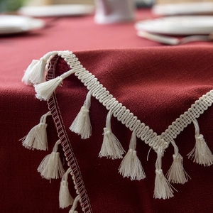 Detail of dark red linen tablecloth featuring elegant white tassel fringe and fabric texture