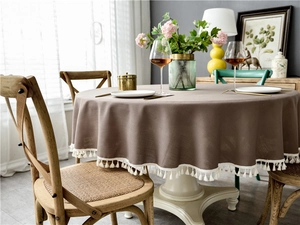 Detail of coffee brown round tablecloth featuring white decorative fringe and linen texture