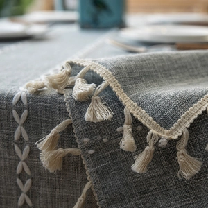 Macro detail of grey textured tablecloth featuring white tassels and fringe edging