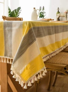 Close-up of yellow and gray striped waterproof linen tablecloth with white tassel fringe