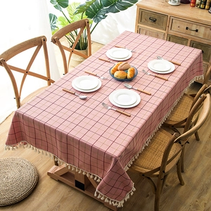 Detail of pink plaid tablecloth with white fringe tassels on a wooden dining table
