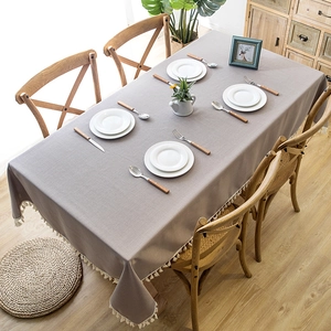 Taupe rectangle tablecloth with white fringe tassels on a wooden dining table