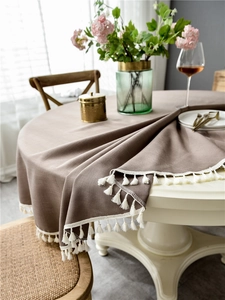 Close-up detail of grey round tablecloth with elegant white fringe tassels and linen texture