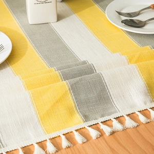 Detail of Nordic striped table runner with yellow tassels and coarse linen fabric texture
