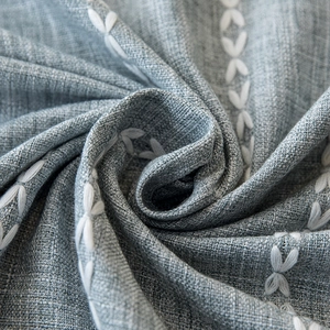 Close-up of blue linen tablecloth featuring white embroidered leaves and fringe texture