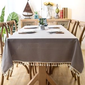 Detail of greyish-brown rectangular tablecloth with ivory tassels on a wooden table