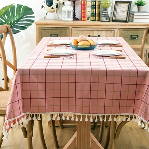 Detail of pink plaid waterproof tablecloth featuring white tassels on a rustic wooden table