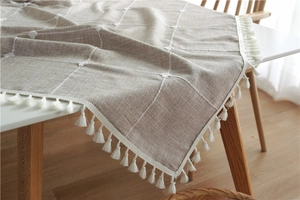 Detail of plaid cotton linen tablecloth with elegant white tassels on a wooden table