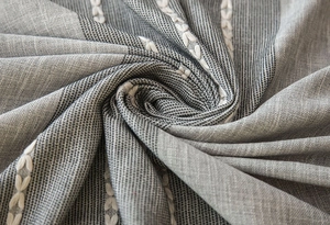 Close-up of grey jacquard tablecloth fabric with white embroidery and fringe detail