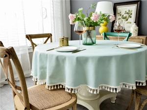 Close-up of light blue round tablecloth with woven texture and white fringe tassels