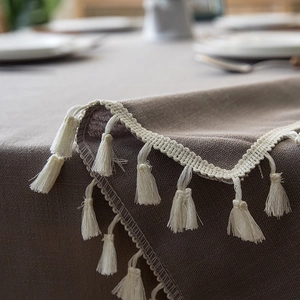 Detailed view of beige linen tablecloth featuring decorative cream fringe edges and texture