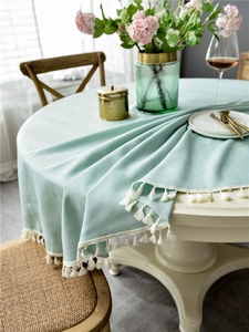 Detail of mint green round tablecloth with white fringe trim and soft linen texture