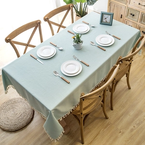 Detail of light green faux linen tablecloth with white tassel trim in a Nordic dining setting
