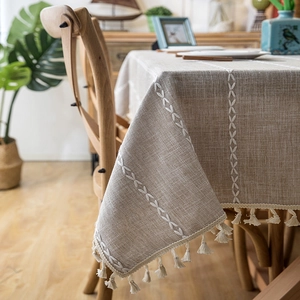 Close-up of beige linen texture tablecloth featuring white fringe edges and embroidery
