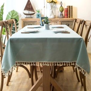 Close-up of light green linen-style tablecloth featuring elegant white cotton tassels