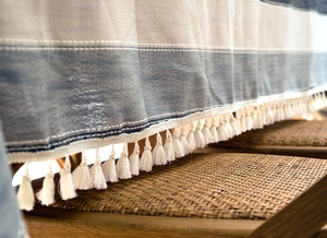 Close-up of textured blue striped linen tablecloth featuring decorative white tassels
