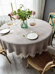 Detail of light grey round tablecloth featuring delicate white fringe tassels on edges