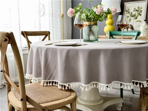 Detail of round grey tablecloth featuring delicate white fringe tassels and linen texture