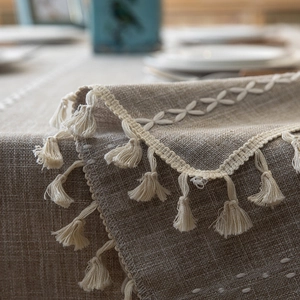 Detail of linen tablecloth with white cross-stitch embroidery and tassel fringe