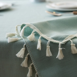 Detail of mint green linen tablecloth featuring white tassel fringe and woven texture