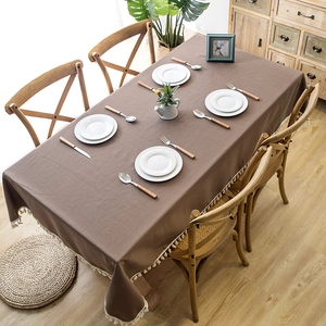 Detail of coffee brown linen tablecloth featuring white tassel fringe on wooden table