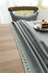 Detail of grey polyester-cotton tablecloth featuring colorful geometric lace trim and texture