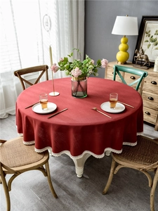 Detail of burgundy round tablecloth with white wavy lace fringe and woven texture