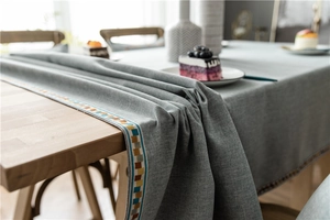 Detail of grey polyester-cotton tablecloth with colorful mosaic webbing trim on wood