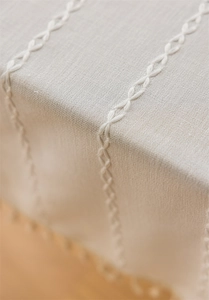 Close-up of cream linen tablecloth featuring white embroidered patterns and fine texture