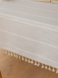 Detail of cream linen tablecloth featuring white wave embroidery and elegant fringe edges