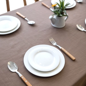 Brown faux linen tablecloth with fringe edge on table featuring ceramic plates and plants