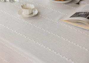 Detail of light beige faux linen tablecloth featuring white embroidered wavy fringe lace