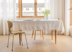 Detail of cream linen tablecloth with elegant fringe tassels and woven texture