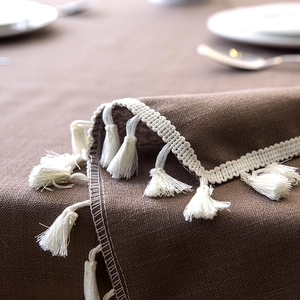Close-up of dark coffee linen tablecloth featuring elegant cream fringe and woven texture