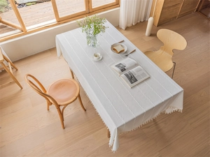 Detail of white linen-textured tablecloth featuring vertical patterns and tassel edge