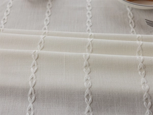 Close-up of beige linen tablecloth with vertical white bow-shaped embroidery and fringe