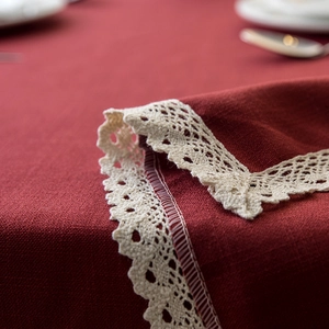 Close-up of deep red linen tablecloth showing intricate cream lace trim and woven texture