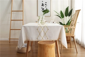 Close-up of geometric gold embroidery on beige linen tablecloth with lace edge
