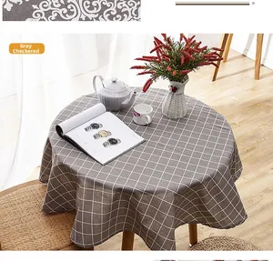 Detail of round grey checkered tablecloth with fringe on a wooden dining table